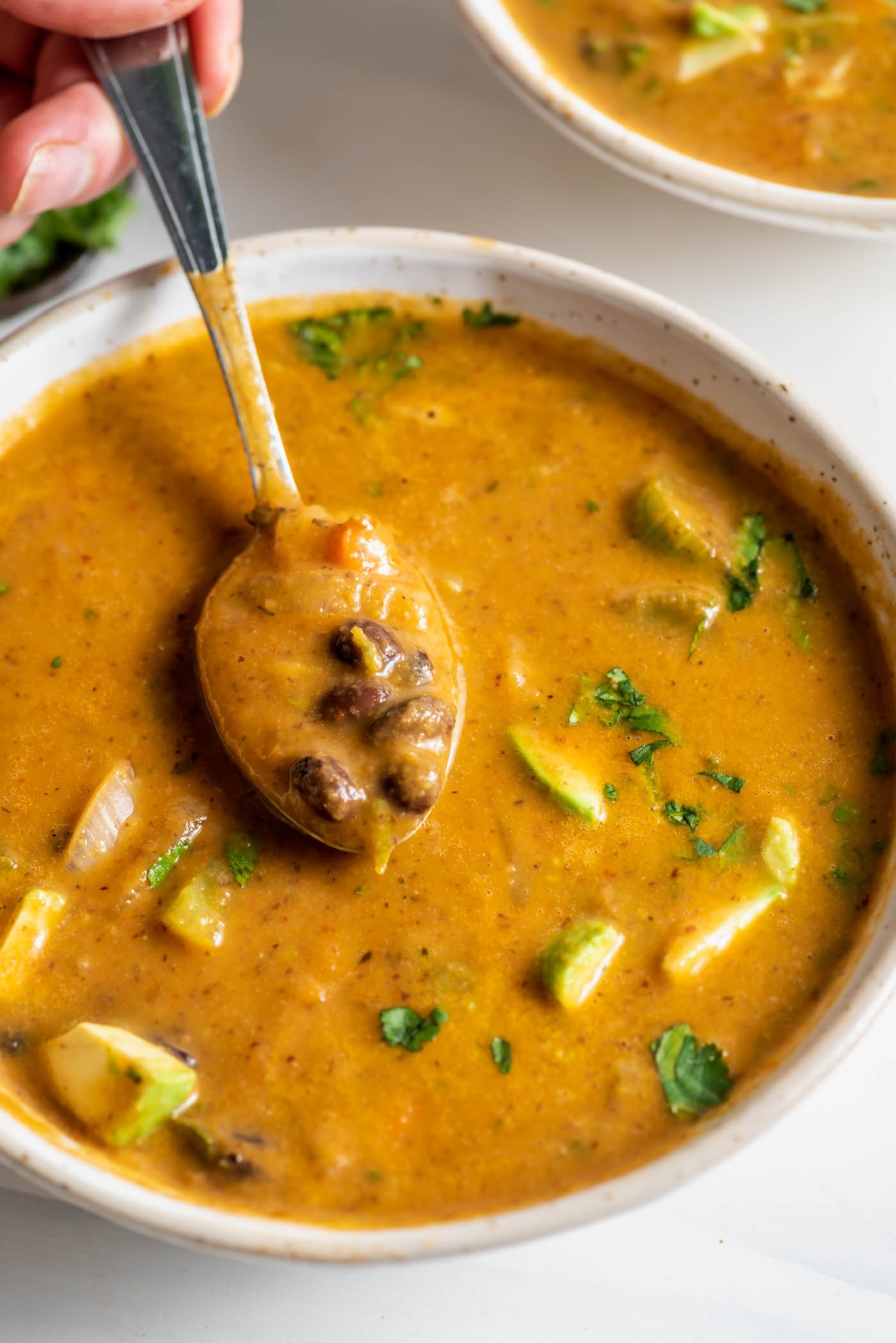 Taking a spoonful of black bean soup from a bowl of soup.