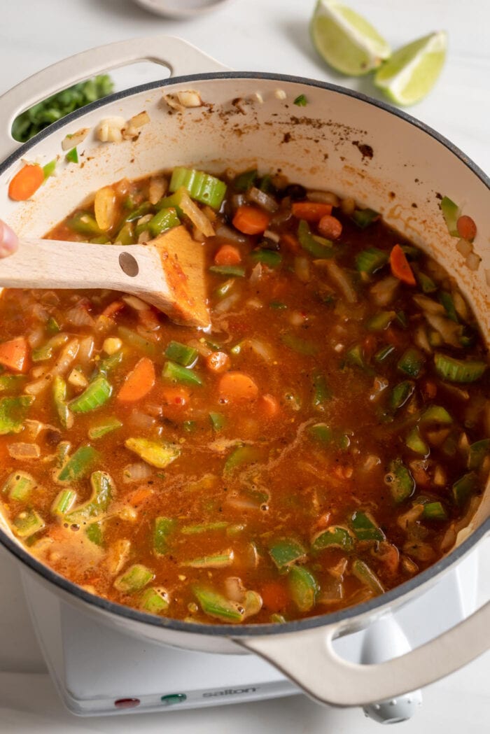 Tomato vegetable soup cooking in a large soup pot with a wooden spoon resting in pot.