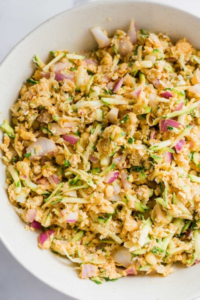 Raw chickpea burger batter with zucchini and red onion in a large mixing bowl.