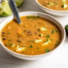 Bowl of black bean soup with avocado in it. Second bowl of soup in background.