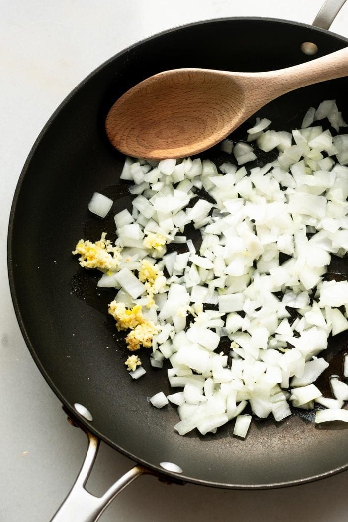 Cooking onions and garlic in a sauce pan for coconut ginger carrot soup.