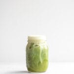 Dairy-free almond milk iced matcha latte in a glass jar against a white background.