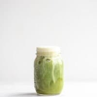 Dairy-free almond milk iced matcha latte in a glass jar against a white background.