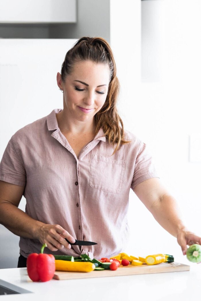 A woman chopping vegetables on a cutting board.