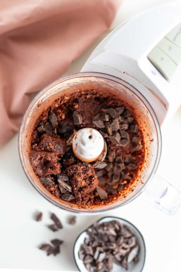 Dark chocolate chunks in a food processor with a thick chocolate dough.