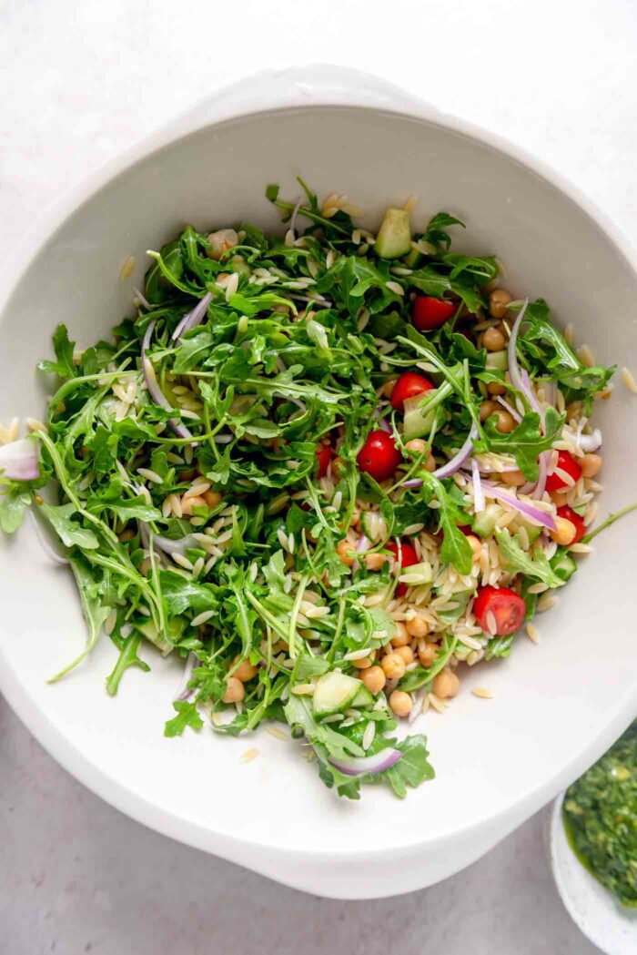 Orzo pesto salad with tomatoes and chickpeas in a large mixing bowl.