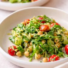 Plate of orzo pesto salad with tomatoes, arugula, red onion and chickpeas.