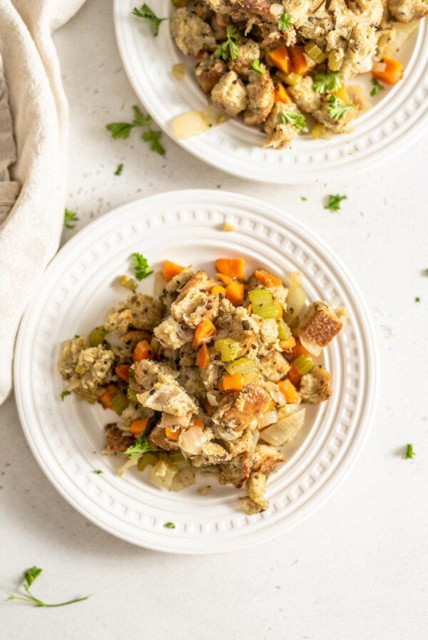 Two small white plates of a serving of plant-based stuffing made with bread and vegetables.