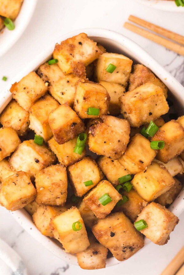 A big bowl of crispy baked tofu cubes sprinkled with green onion.