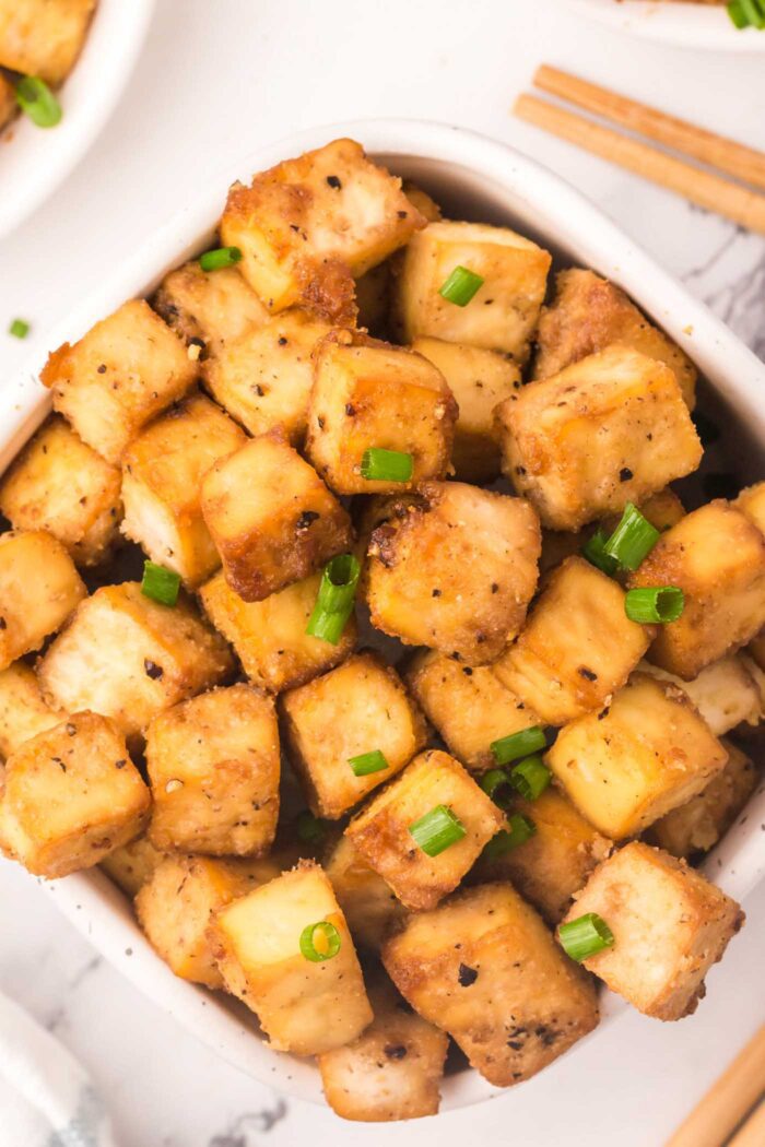A big bowl of crispy baked tofu cubes sprinkled with green onion.