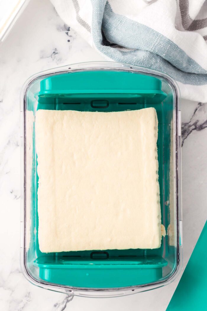 A block of firm tofu in a tofu press.