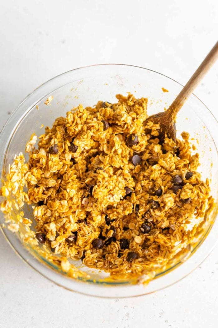 Raw pumpkin cookie dough batter in a glass mixing bowl with a wooden spoon.
