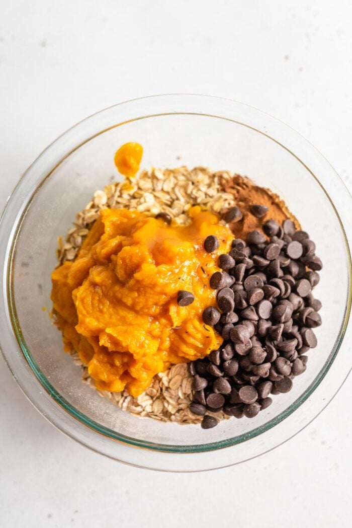 Pumpkin, oats, chocolate chips and cinnamon in a glass mixing bowl.