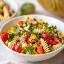 Bowl of black bean pasta salad with tomatoes, cucumber, cilantro and corn.