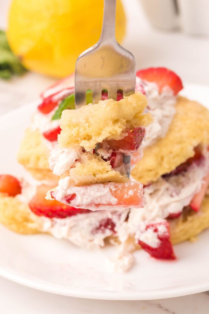 Fork with a forkful of strawberry shortcake biscuit, whipped cream and strawberry.
