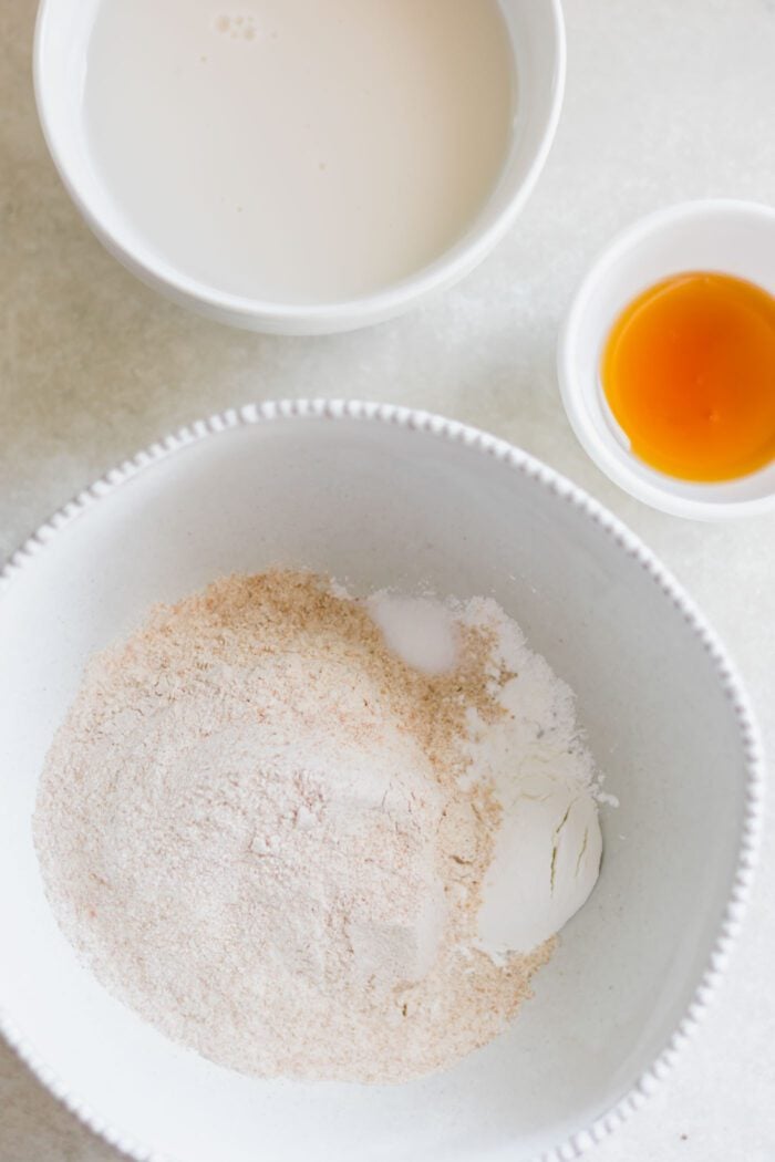 Overhead view of a bowl of dry pancake ingredients in a bowl, a small dish of vanilla and a bowl of almond milk.