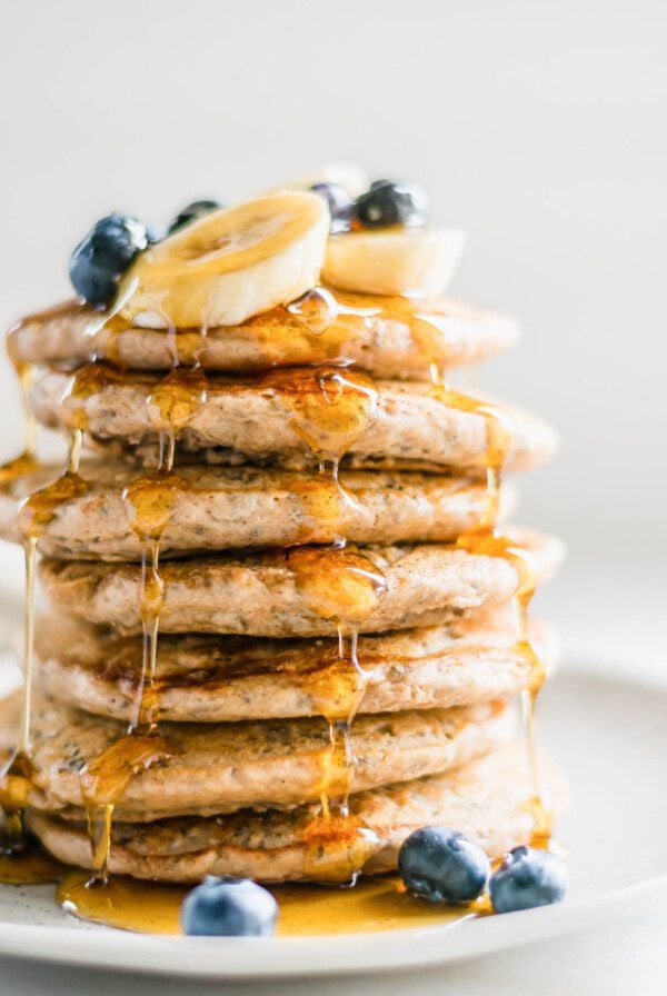 Stack of 7 thick and fluffy chia pancakes topped with maple syrup and blueberries on a plate.