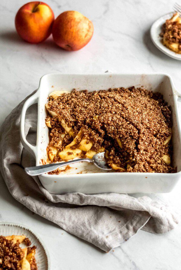 Grain-free vegan apple crisp being scooped out of a white baking dish.