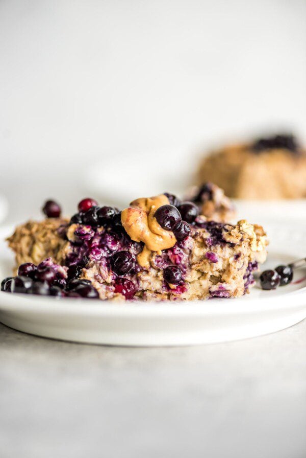 A slice of baked banana oatmeal topped with berries and peanut butter on a plate.