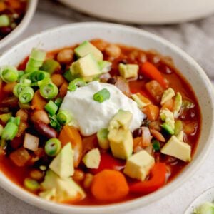 Bowl of three bean chili topped with sour cream, avocado and green onions.