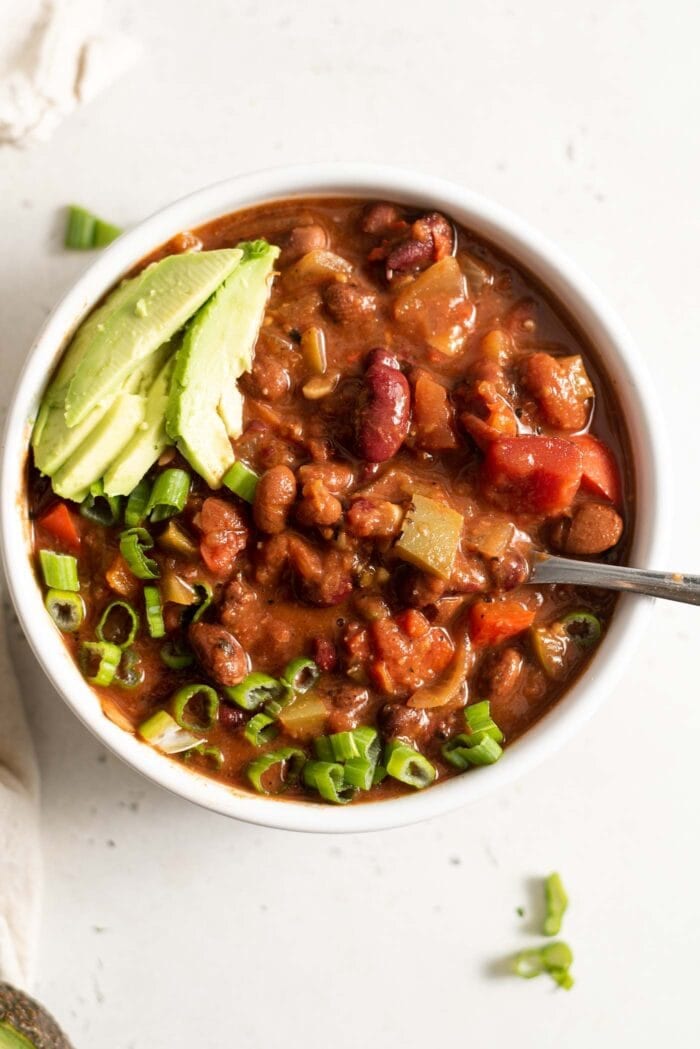 A bowl of vegan chili topped with avocado and green onion.