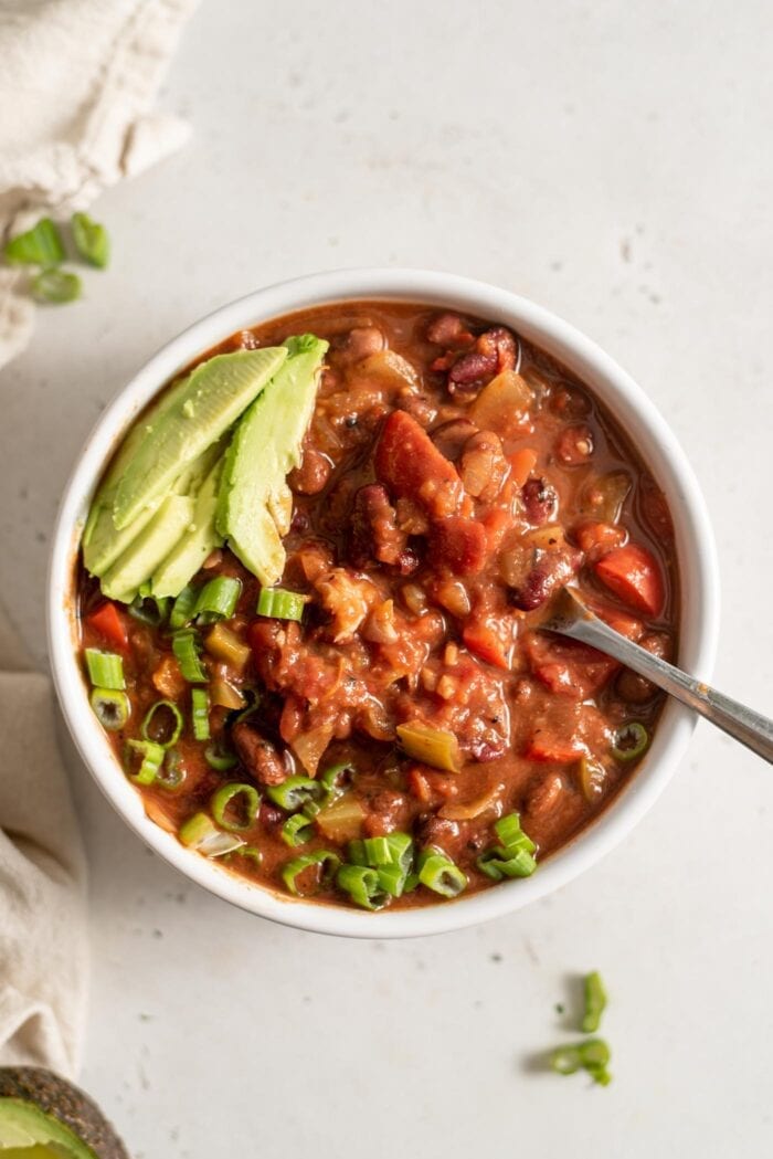 A bowl of vegan chili topped with avocado and green onion.