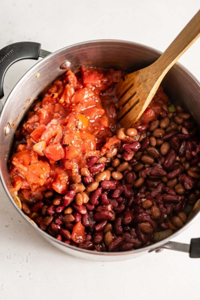 Beans and tomatoes being added to a large soup pot.