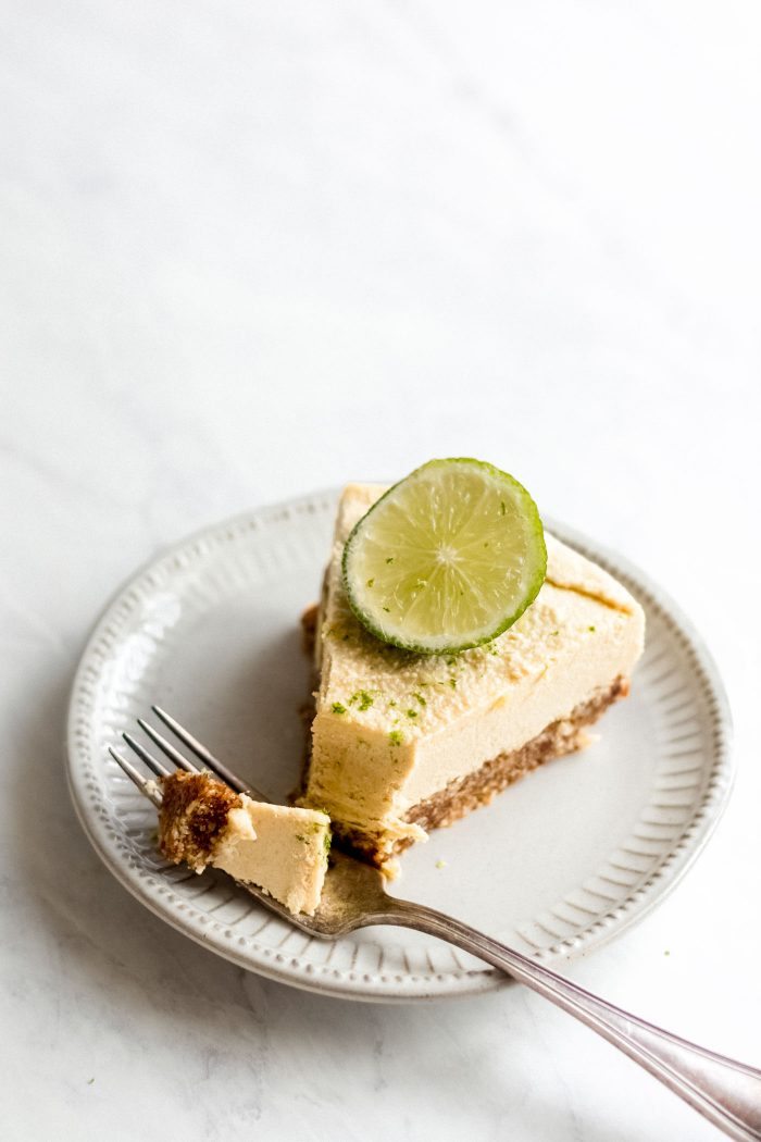 Slice of raw mango cheesecake on a white plate with a fork.