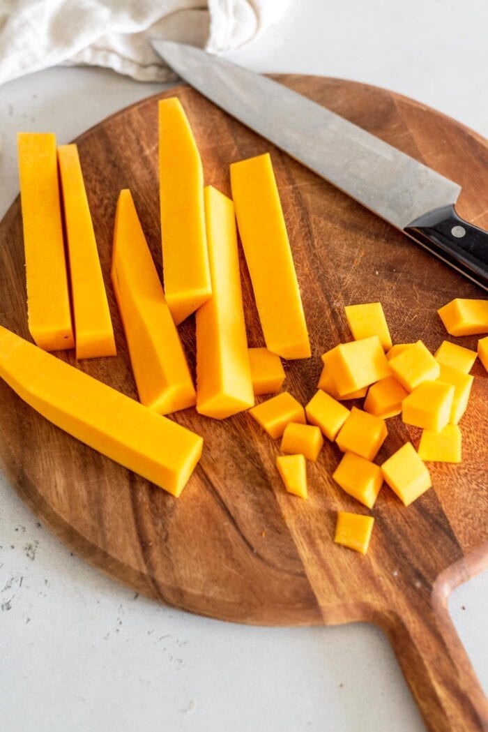 Peeled butternut squash cut into cubes on a cutting board with a knife.