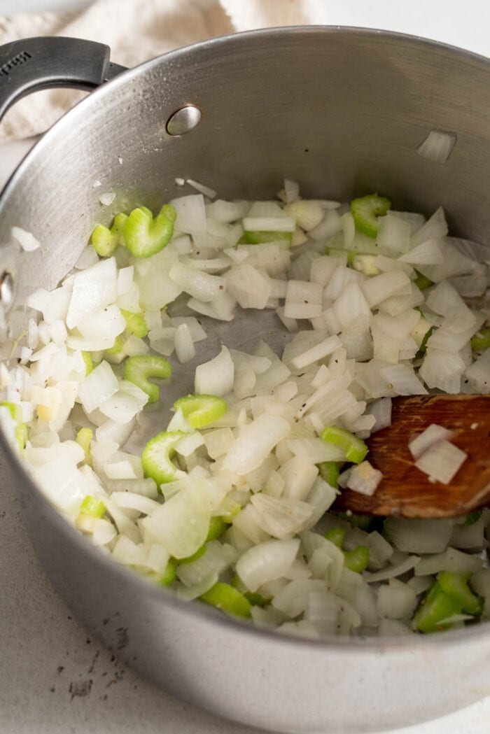 Onion, garlic and celery in a large soup pot with a wooden spoon.