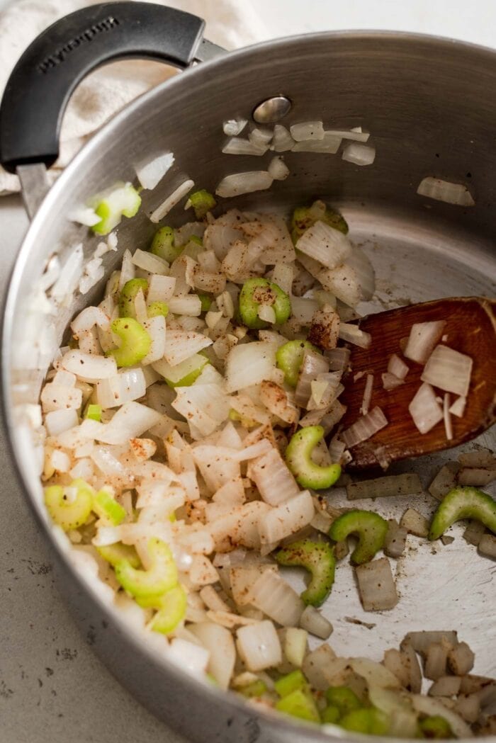 Cumin and curry powder being stirred into celery, onion and garlic in a soup pot.