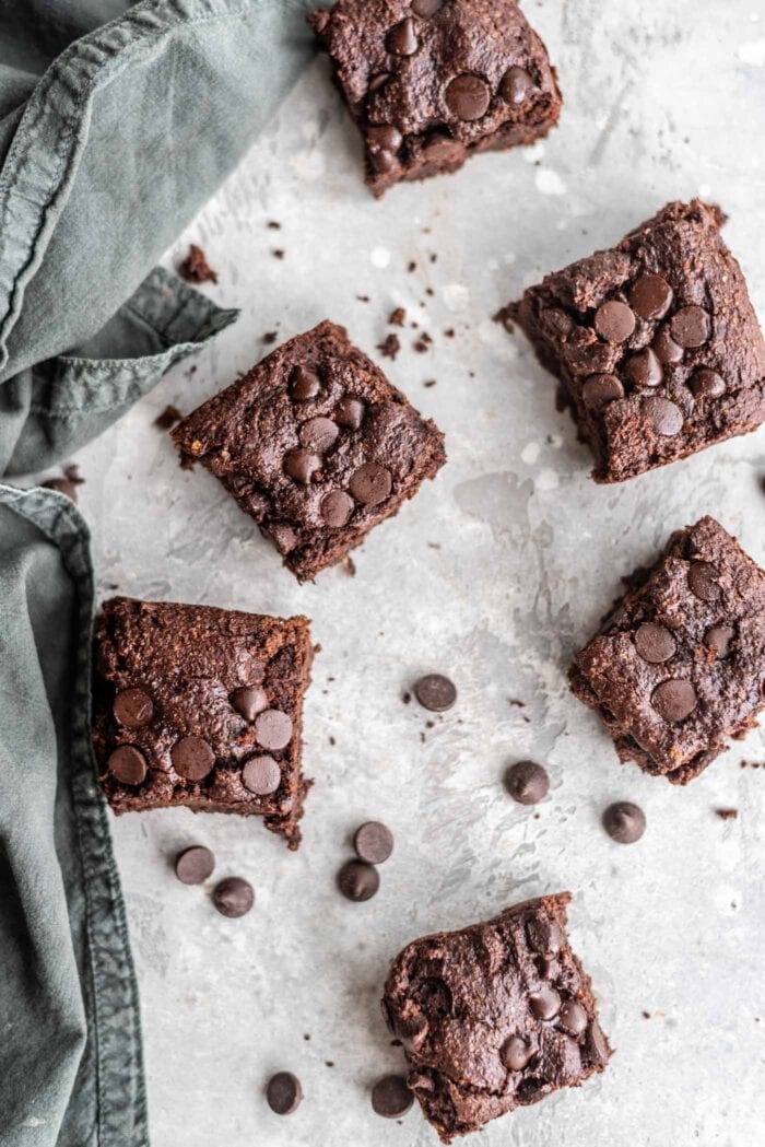 Overhead shot of 6 vegan oat flour brownies on a grey surface scattered with chocolate chips.