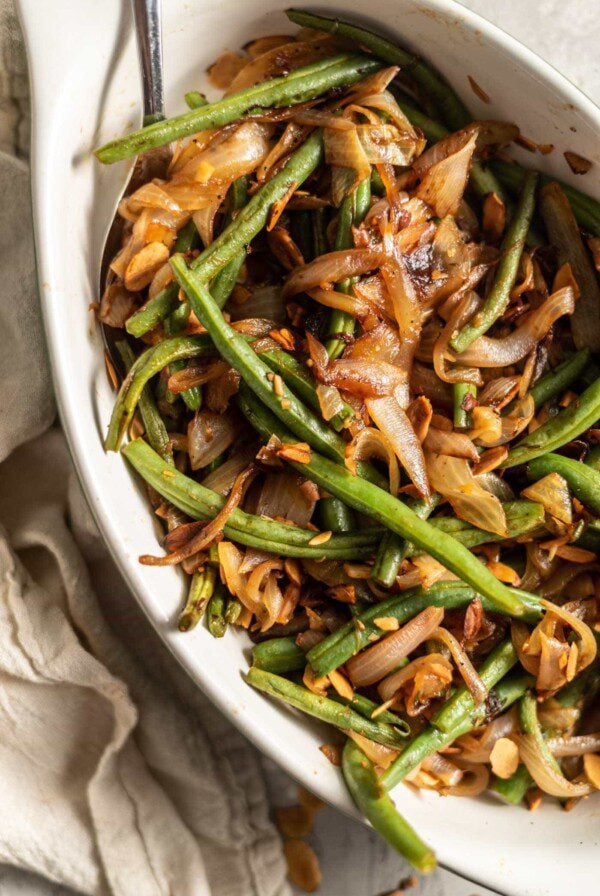Sauteed green beans with onions, garlic and slivered almonds in a serving dish with a spoon.