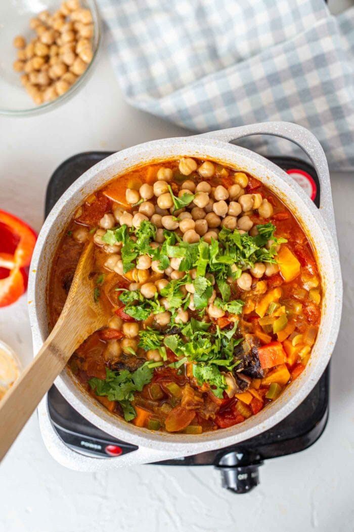 A large pot of stew with cilantro being stirred in.