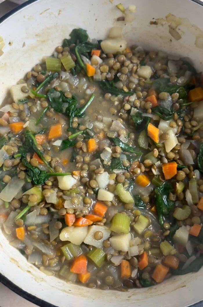 Hearty vegan lentil stew with potatoes cooking in a large pot.
