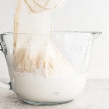 A glass jar of homemade almond milk with a nut milk bag in it.