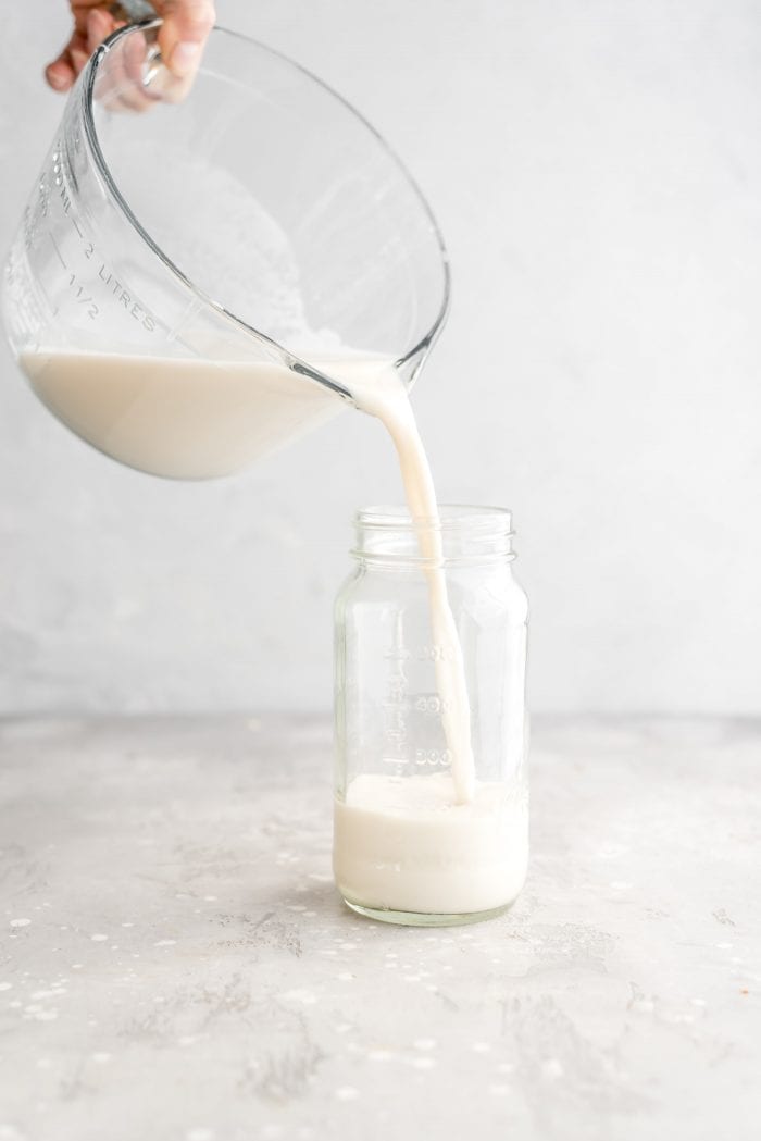 Pouring a homemade oat milk recipe into a glass storage container.