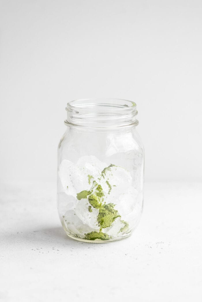 Ice and green tea matcha powder in a small glass mason jar.