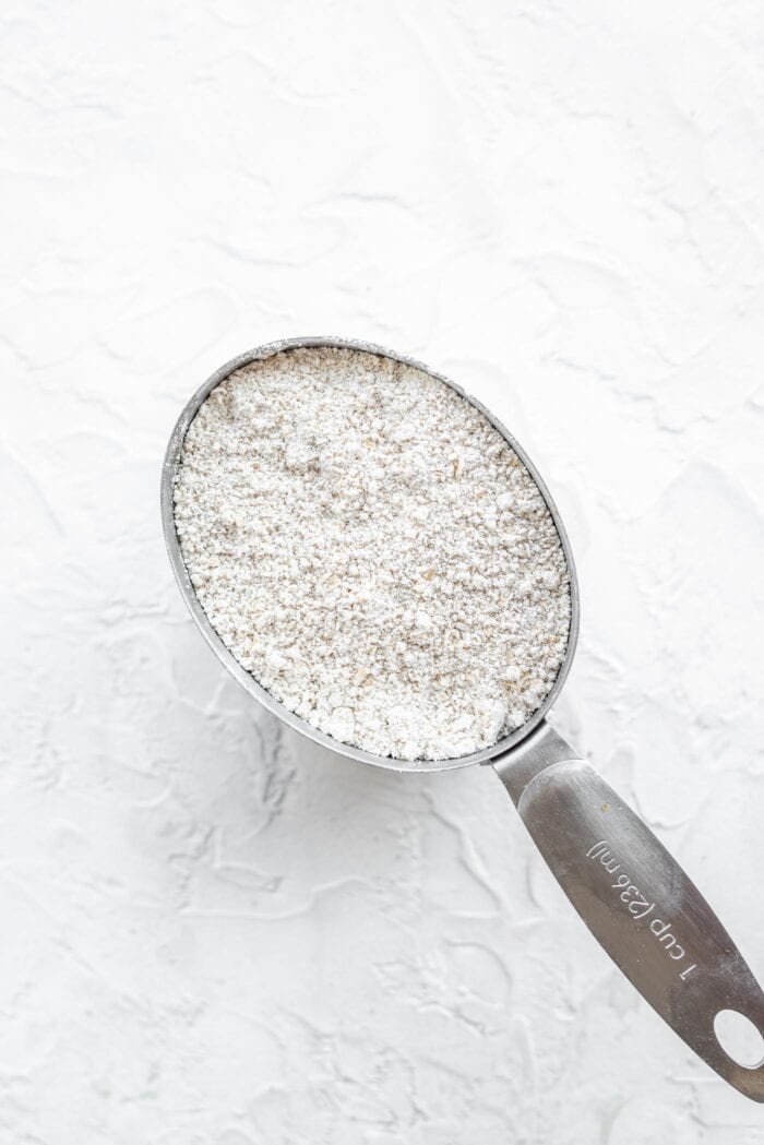 Metal measuring cup with oat flour in it.