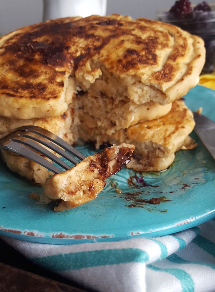 Fork with piece of pancake on it on a plate with a stack of pancakes on it.