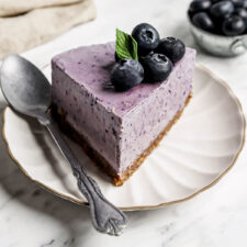 Slice of blueberry cheesecake on a small plate with a spoon.