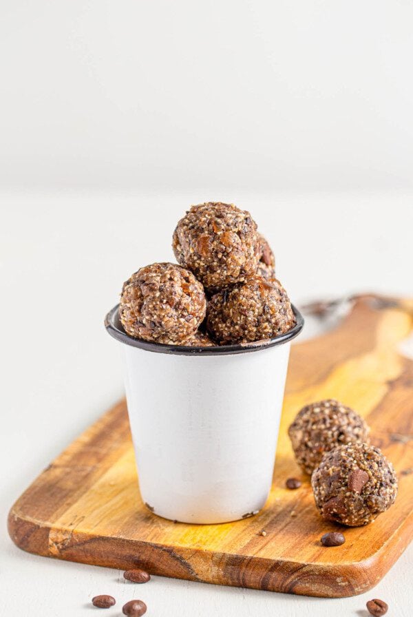 Small cup filled with chocolate energy balls sitting on a cutting board.