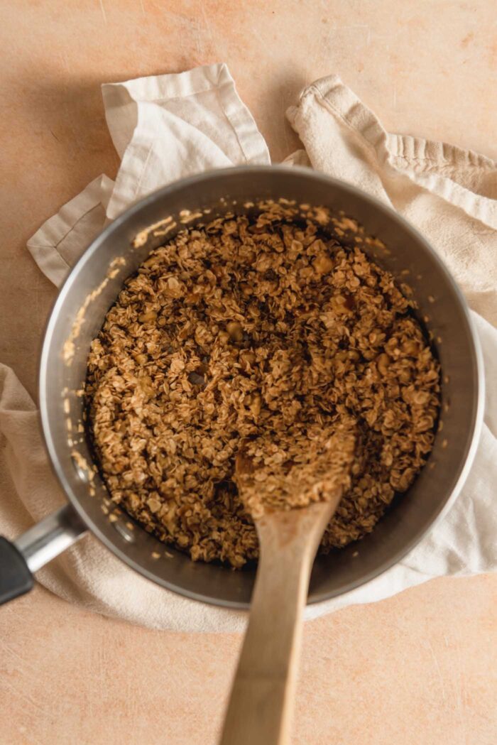 A crumbly, dough oat mixture in a small pot with a wooden spoon resting in it.