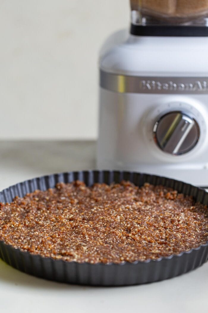 A pecan and date raw pie crust in a shallow pie dish.