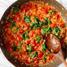 Large pan of tomato orzo with spinach with a wooden spoon resting in pan.