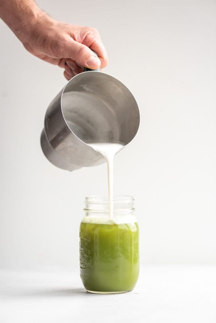 A hand pouring foamed almond milk into matcha in a jar using the Breville Milk Cafe.