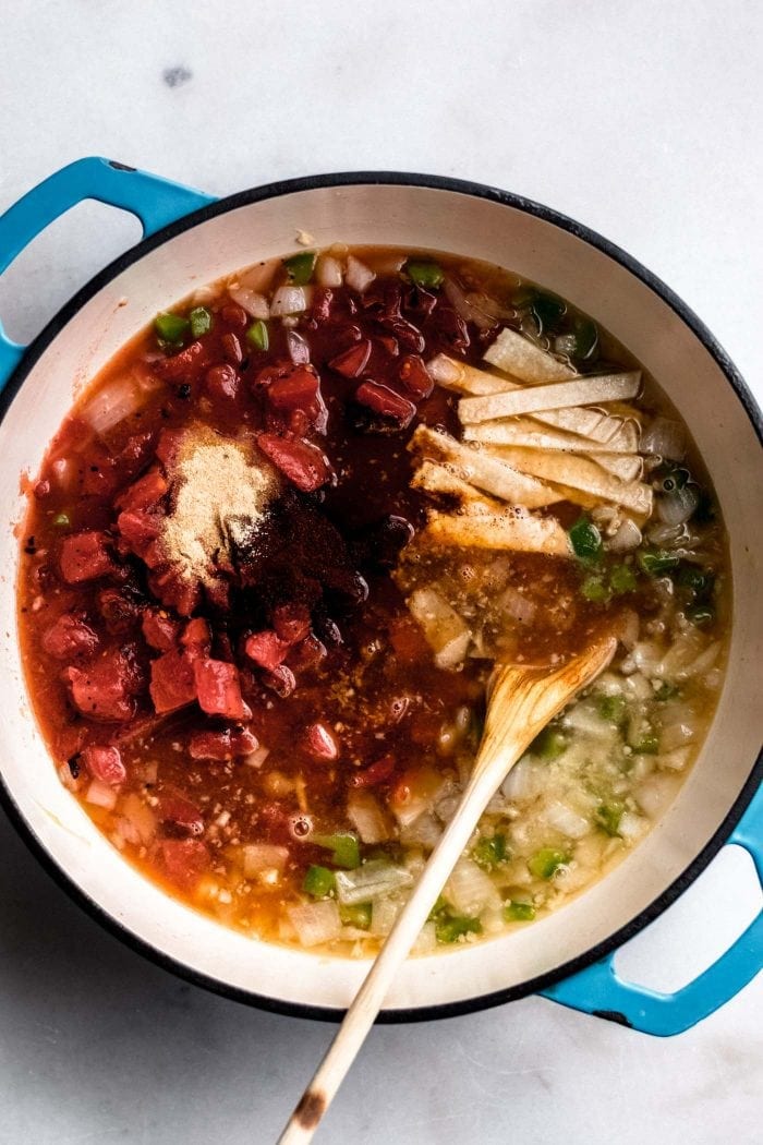 Garlic powder, diced tomatoes, garlic, onion, broth and jalepeno in a soup pot for making vegan tortilla soup.