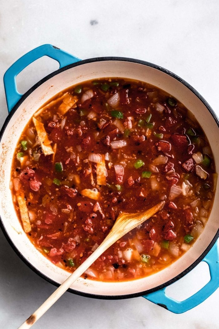 Vegan tortilla soup in a blue soup post with a wooden spoon.