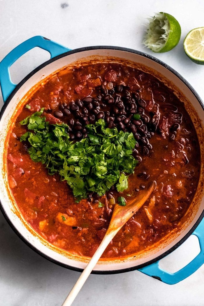 The best vegan tortilla soup in a pot topped with cilantro and black beans and a lime on the side.