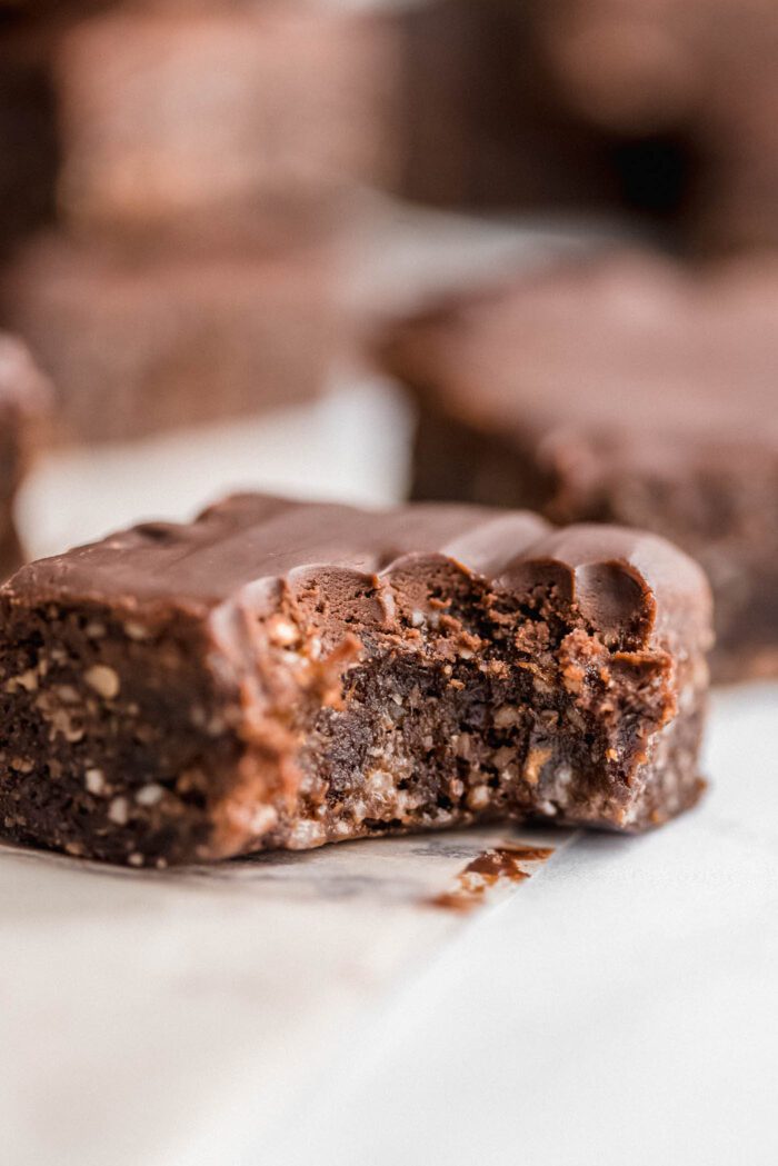 Close up of a no-bake raw hemp brownie topped with chocolate frosting. The brownie has a bite taken out of it showing the texture of the brownie.